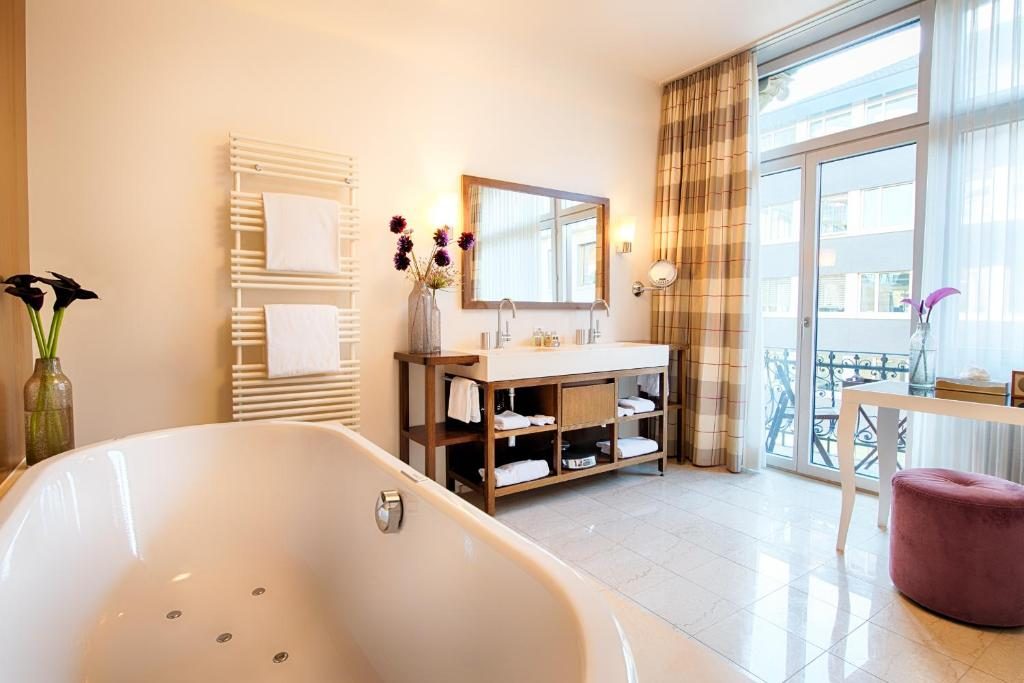 big bath tub in a spacious hotel bathroom with large windows and mirror
