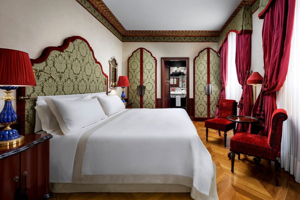 big white bed in a bedroom hotel danieli with red curtains and murano lamps