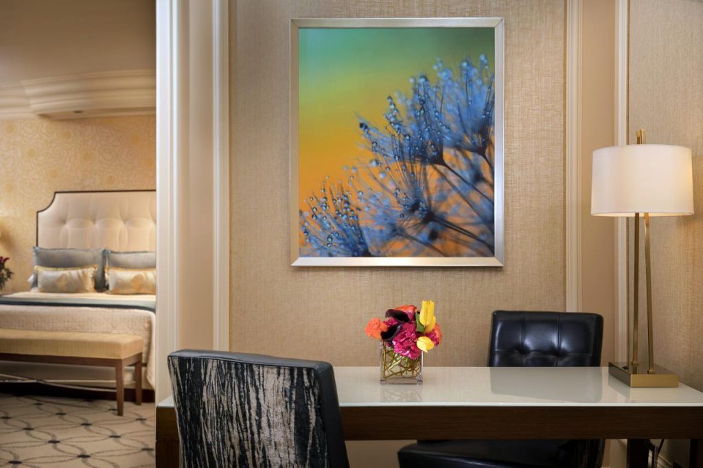 work area in a hotel living room with colored painting hanging the wall and sneak peak view into the bedroom